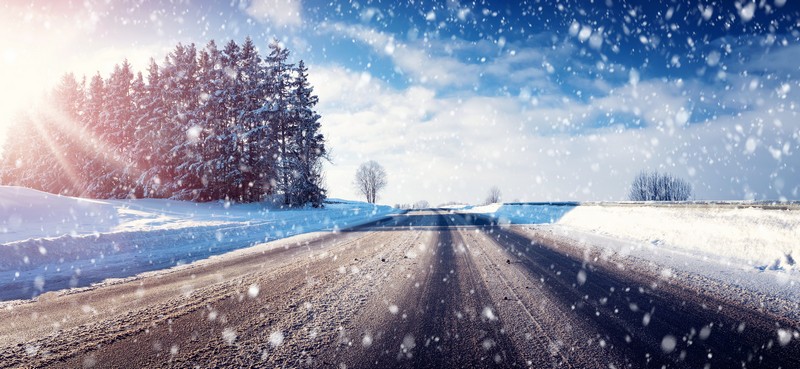 Schneefahrbahn mit Sonnenschein und Schneefall